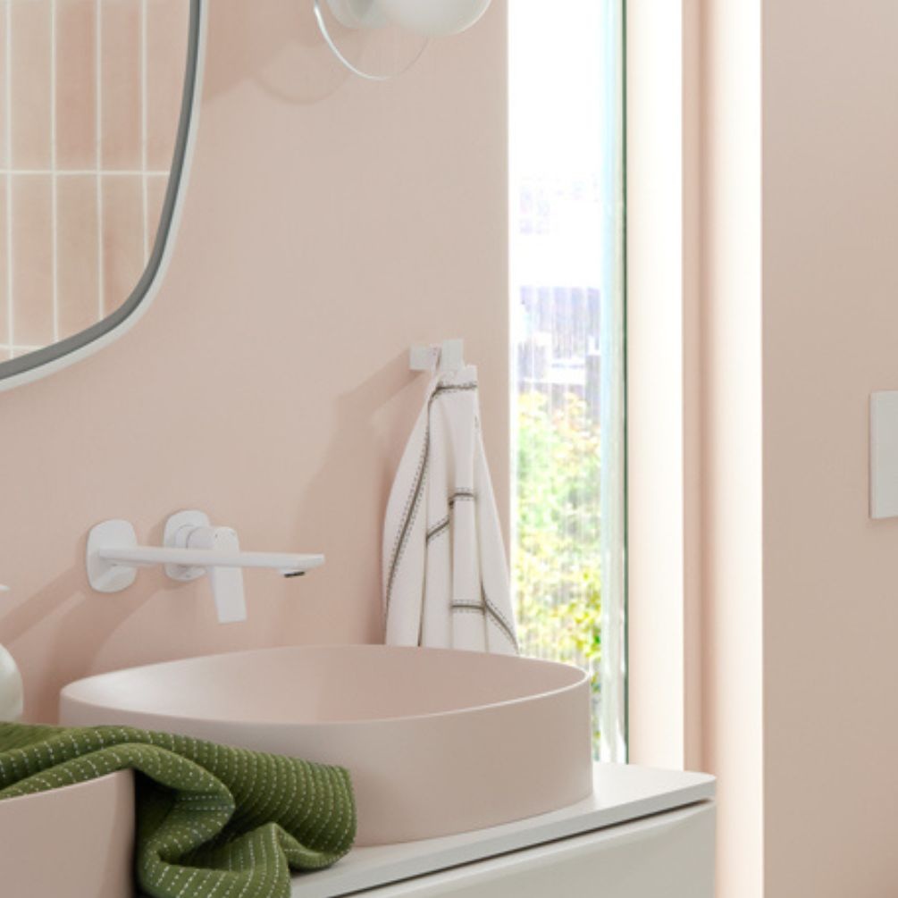 product lifestyle image of vado cameo matt white robe hook hanging white towel next to countertop basin and wall mounted tap in beige bathroom MUS-186-MW